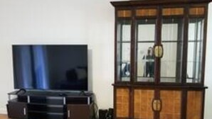 Ein Zimmer mit einem Holfachschrank, einem Flachbildfernseher auf einem Standfuß und einem Deckenventilator.
