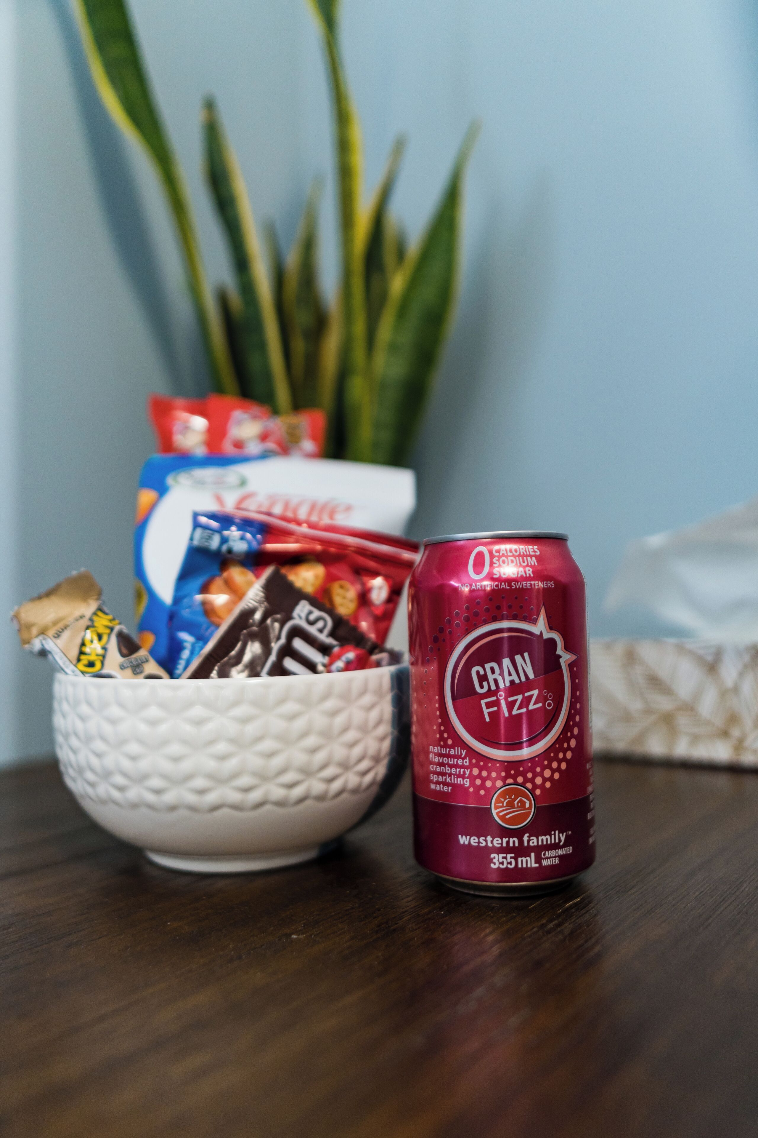 A white bowl filled with snacks and a can of Cran Fizz on a wooden surface.