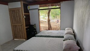 A room with two beds, a wooden door, and a window with a view of trees and a motorcycle outside. - HOSTEL MAKTUB (Santa Rita)