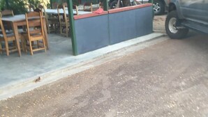A covered outdoor seating area with tables and chairs, a building with a red roof in the background, and a parked vehicle. - HOSTEL MAKTUB (Santa Rita)