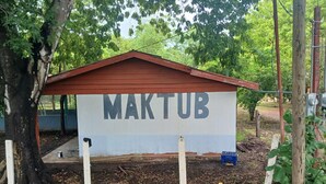 A building with a sign that reads "MAKTUB" in a rural setting with trees and a dirt ground. - HOSTEL MAKTUB (Santa Rita)