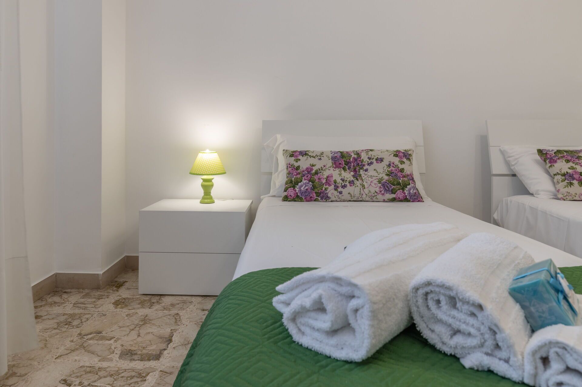 A hotel room with a bed, a nightstand with a lamp, and a green quilted bedspread.