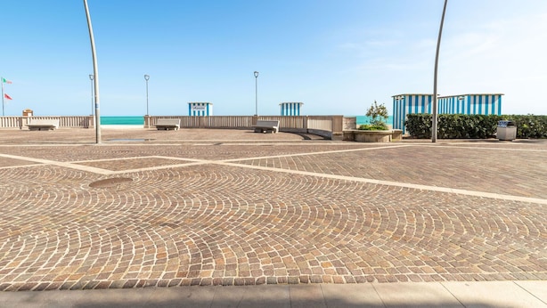 Une promenade dallée offrant une vue dégagée sur la mer, agrémentée de bancs et bordée d’un bâtiment aux rayures bleues portant l  ’inscription « Annite ».