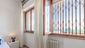 Une chambre à coucher comprenant un lit, une table de chevet, une lampe, une fenêtre donnant sur la plage et un radiateur.
