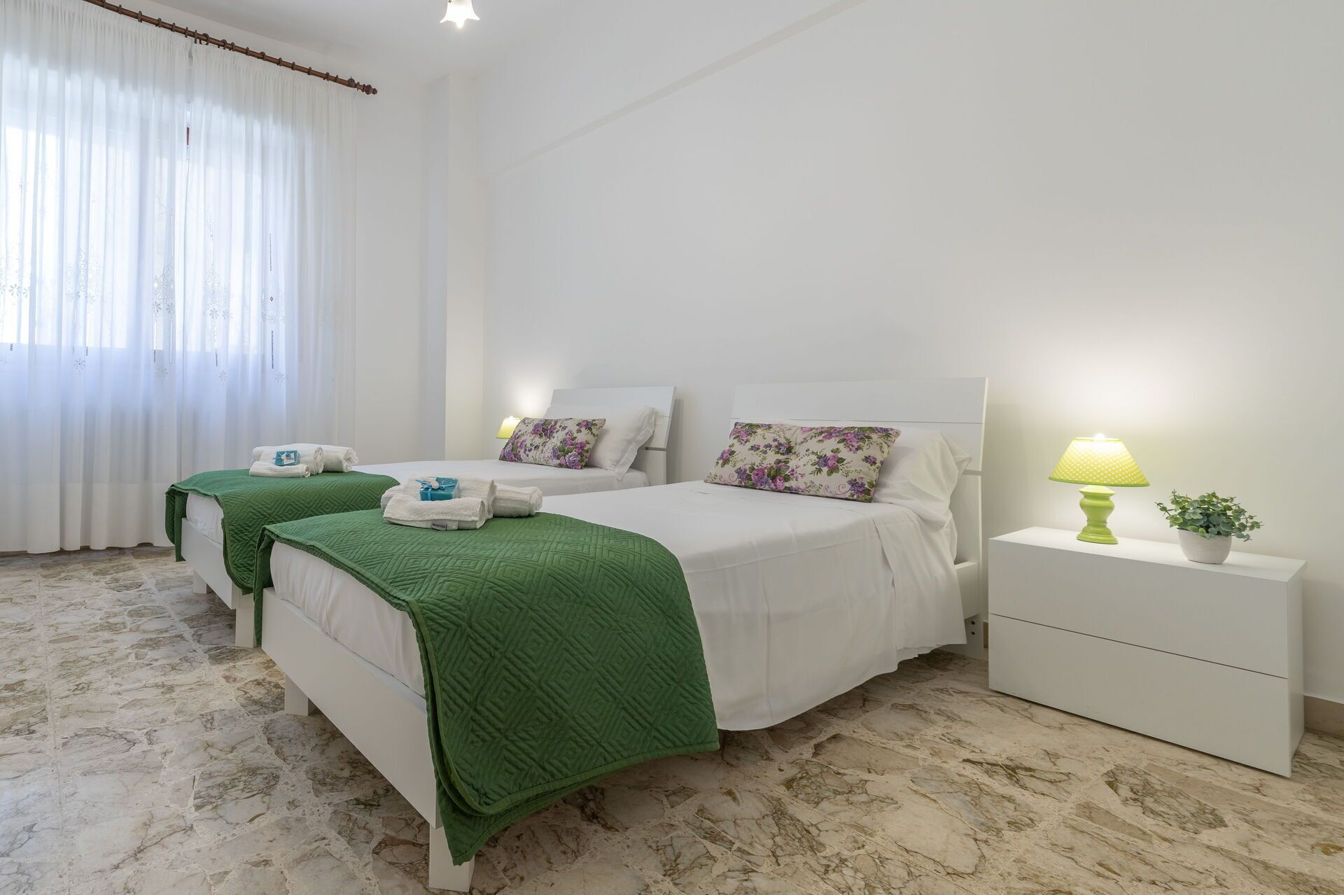 A hotel room with two beds, a nightstand with a lamp, and a potted plant.