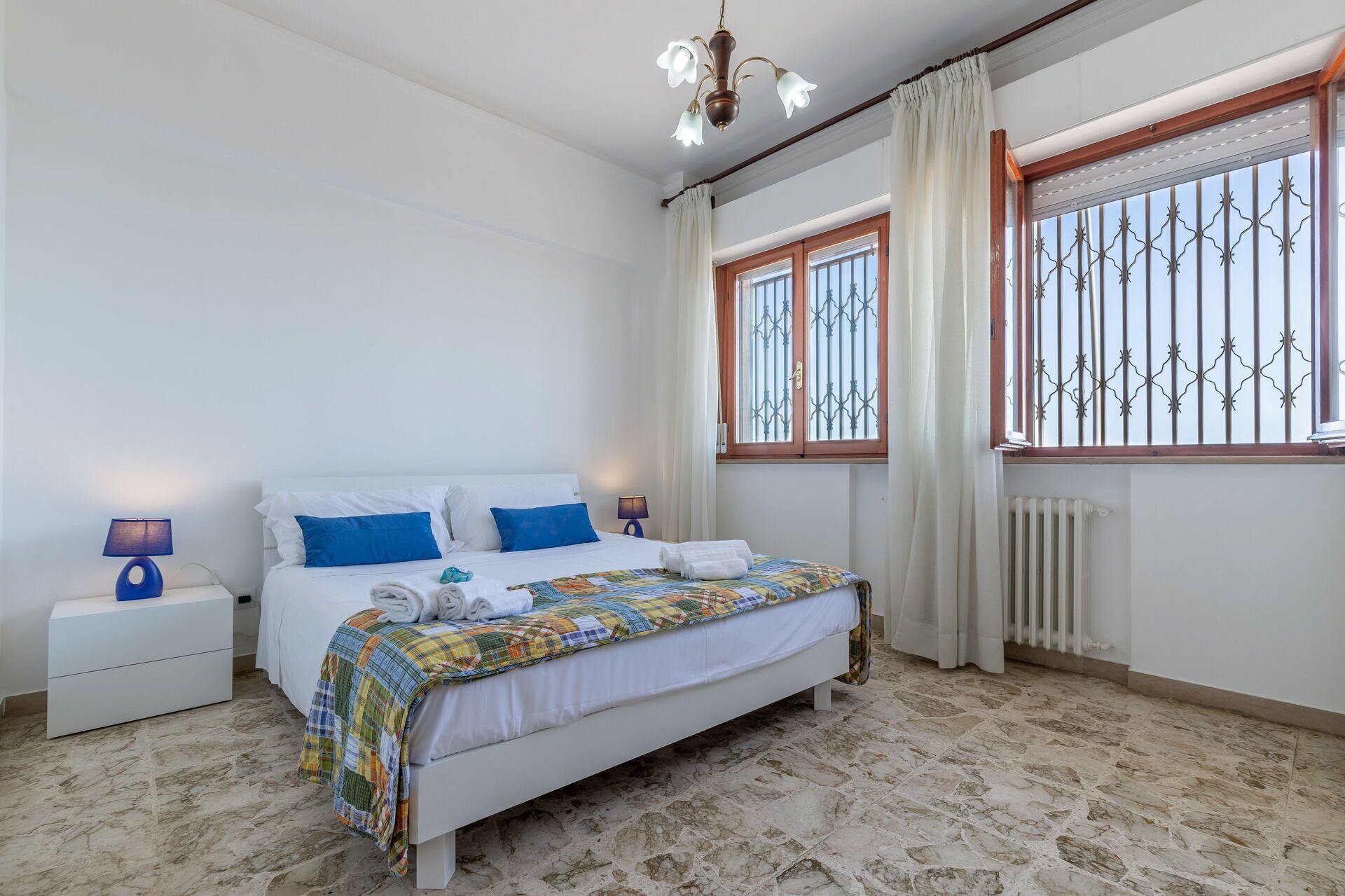 A bedroom with a bed, nightstands, a window with bars, and a radiator.