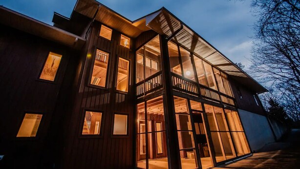 Une maison moderne en bois, dotée de nombreuses fenêtres et d’un balcon.
