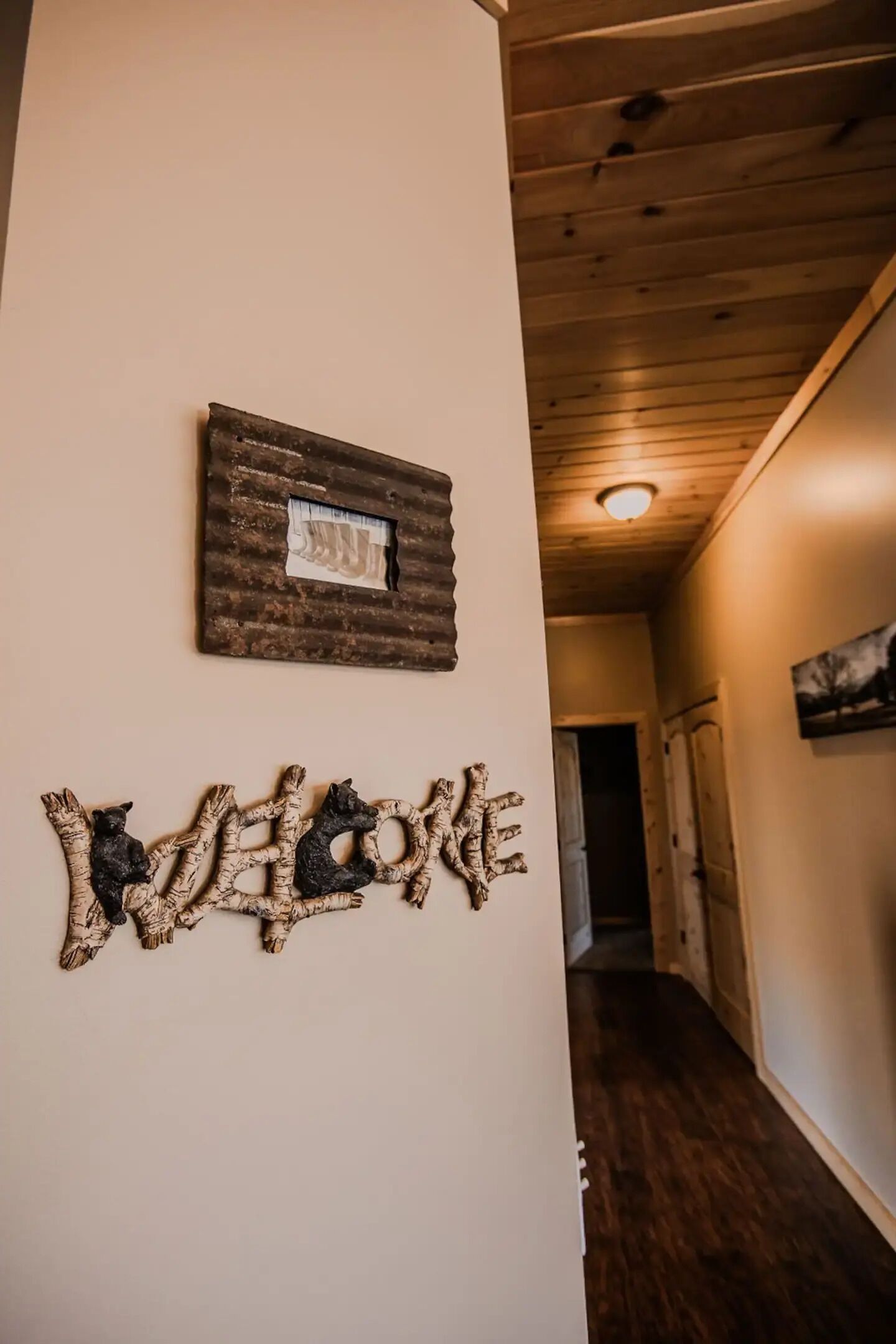 A hallway with wooden flooring, a welcome sign, and a framed picture on the wall.