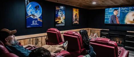 A cinema room with red reclining seats, a large screen, and movie posters on the wall.