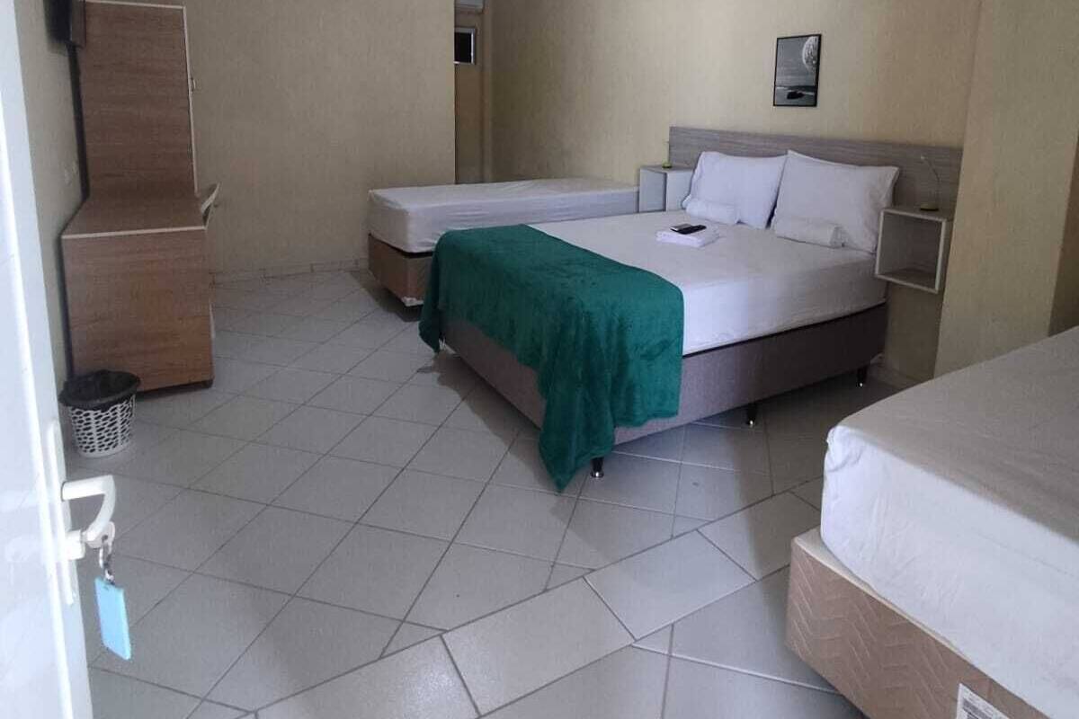 A room with two beds, a wooden cabinet, a small trash bin, and a ceiling light.
