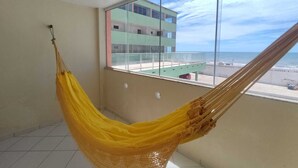 A room with a hammock by a large window overlooking a beach and a building. - Amazônia Praia Hotel (Tibau)