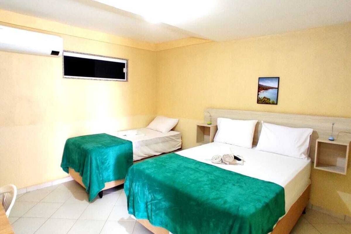 A hotel room with two single beds, a small table, a chair, a window, and a picture on the wall.