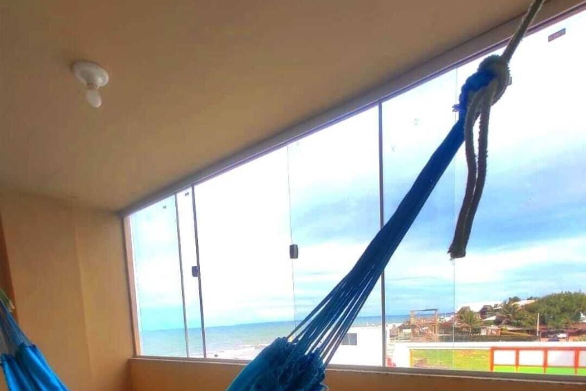 A hammock in a room with a large window overlooking a beach.