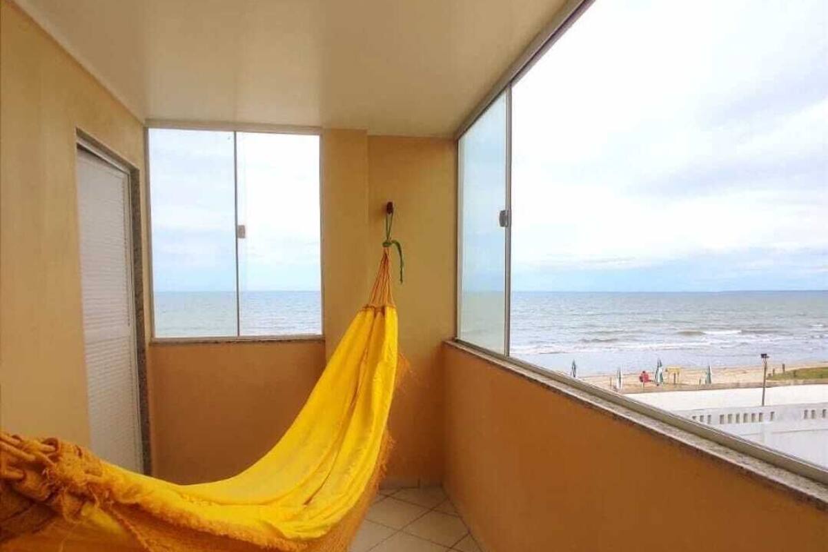 A balcony with a yellow hammock, a view of the sea, and tiled flooring.