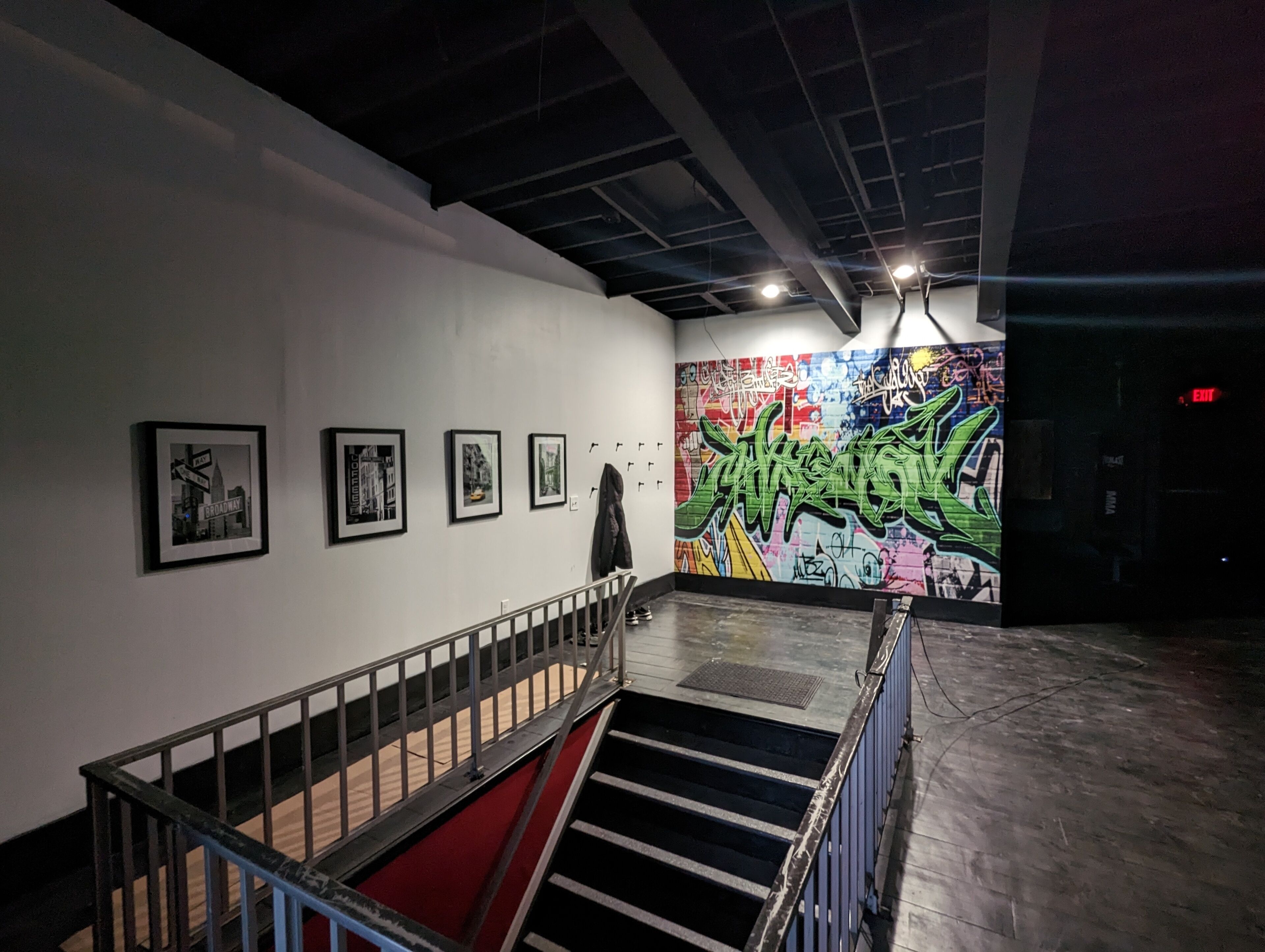 Eine Kunstgalerie im Innenbereich mit gerahmten Bildern an der Wand, einer Treppe und einer Wand mit Graffiti.
