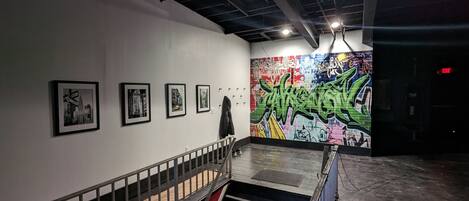 Eine Kunstgalerie im Innenbereich mit gerahmten Bildern an der Wand, einer Treppe und einer Wand mit Graffiti.