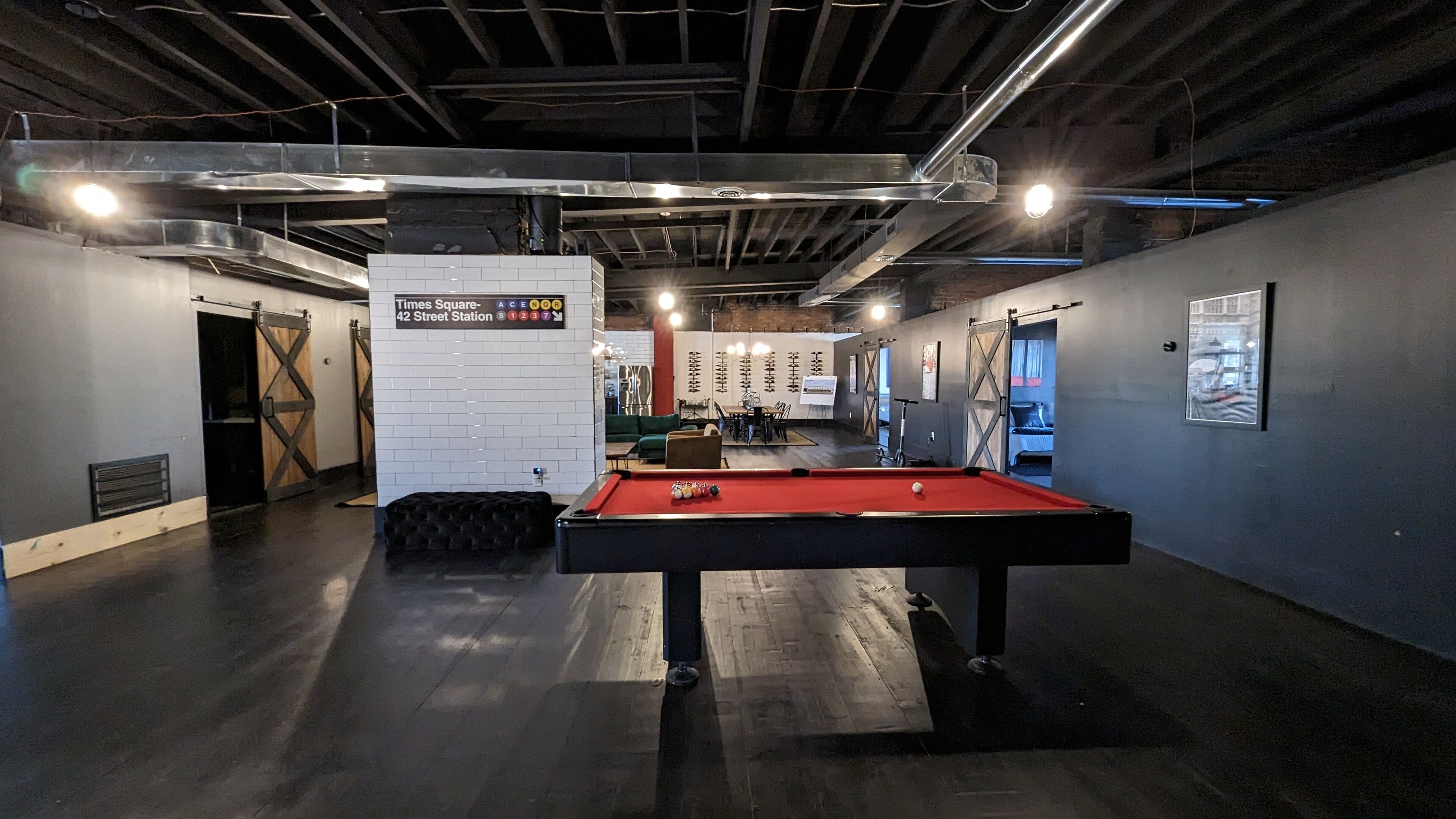 A billiards table in a room with a high ceiling and exposed beams, a seating area with a table and chairs, and a wall with a Times Square sign.