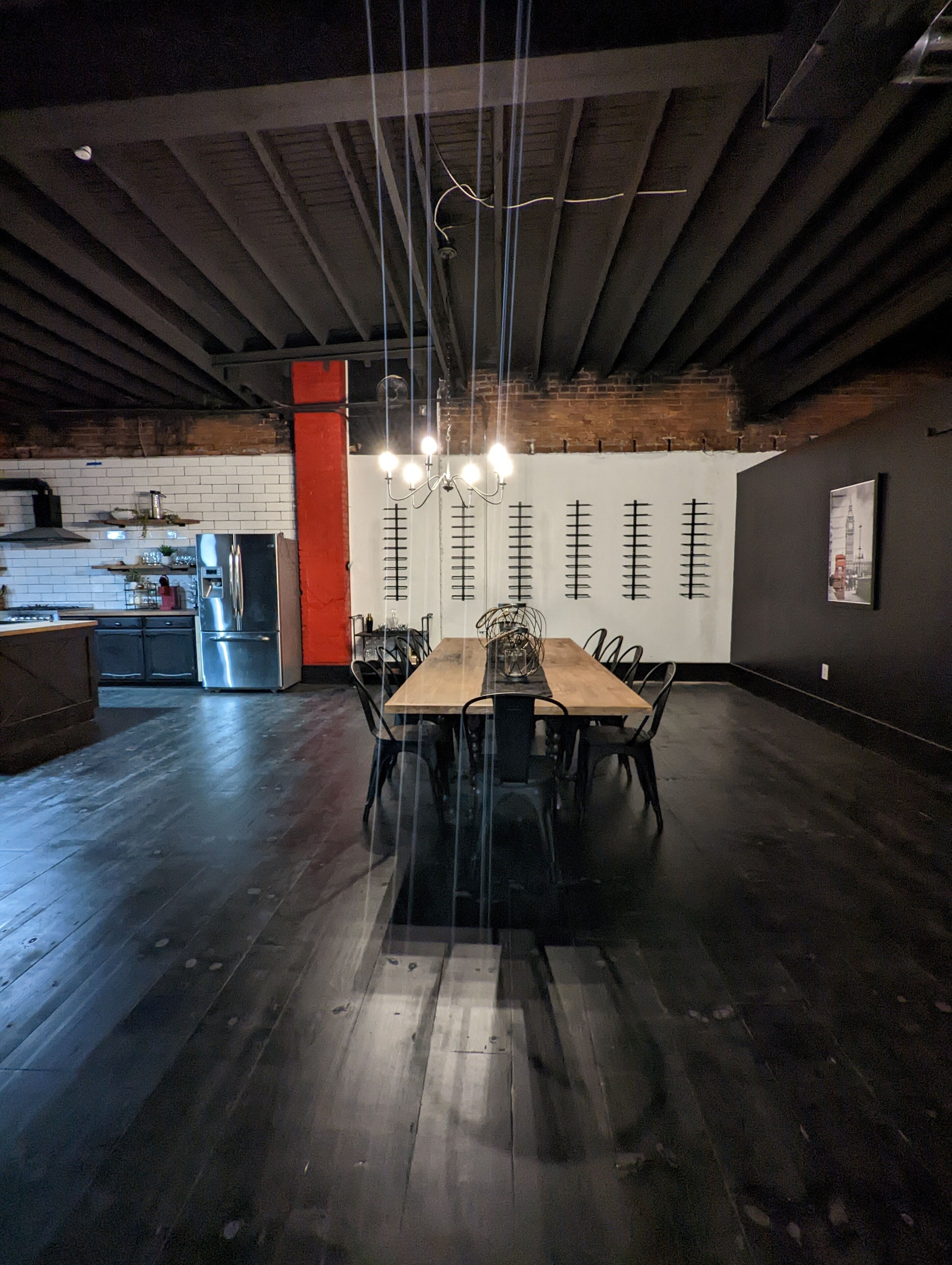 A spacious dining area with a long wooden table and chairs, a chandelier, and a kitchen in the background.