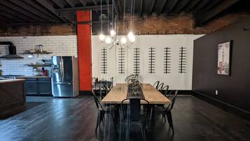 A spacious dining area with a long wooden table and chairs, a chandelier, and a kitchen in the background.