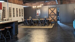 A spacious room with a long table and chairs, a brick wall, and a large wooden door. - Industrial urban Loft within 5 minutes from downtown (Highland Park)