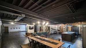 A spacious dining area with a long wooden table and chairs, a sofa, and a kitchen area with a refrigerator and sink. - Industrial urban Loft within 5 minutes from downtown (Highland Park)