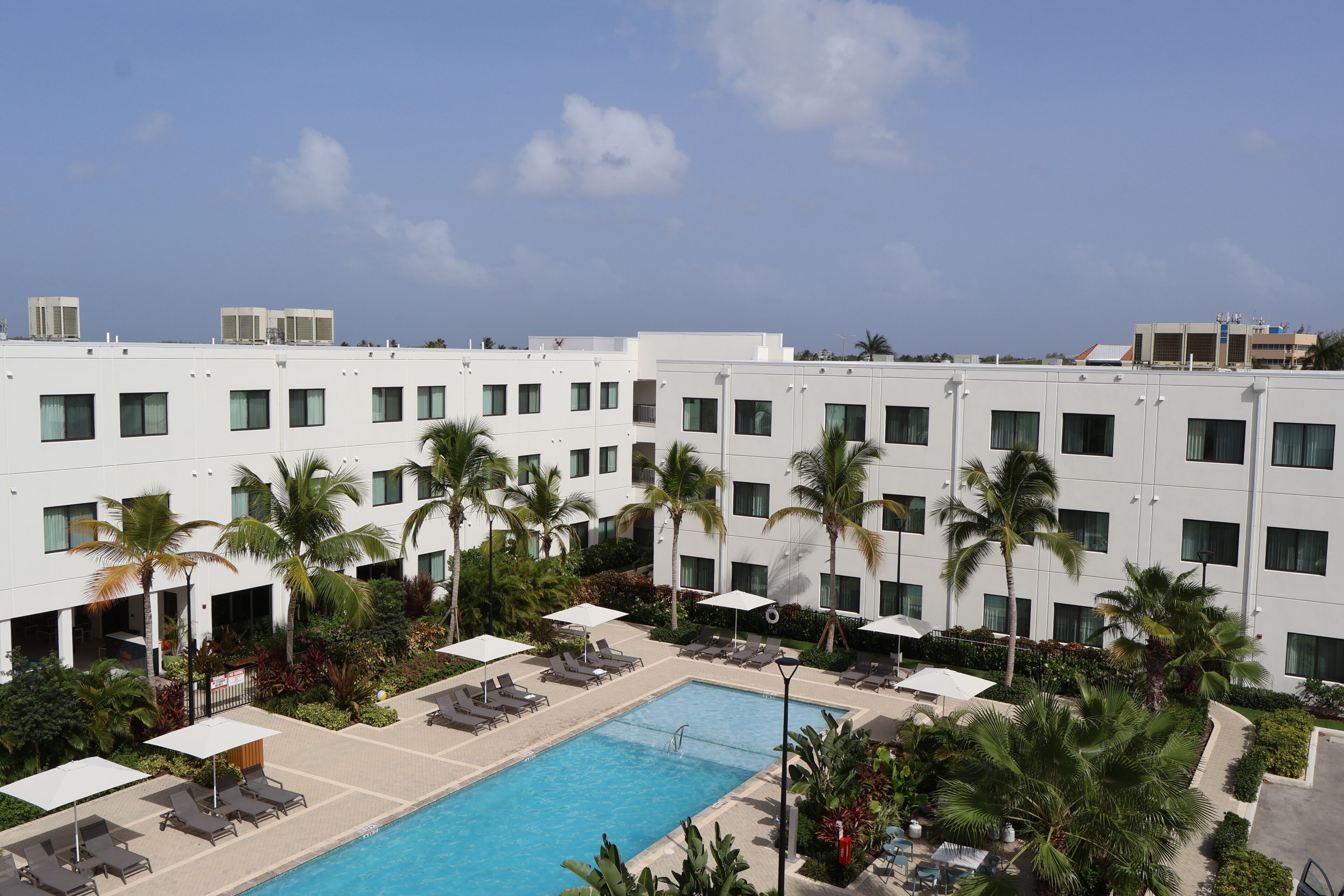 A hotel with a swimming pool surrounded by palm trees and sun loungers.