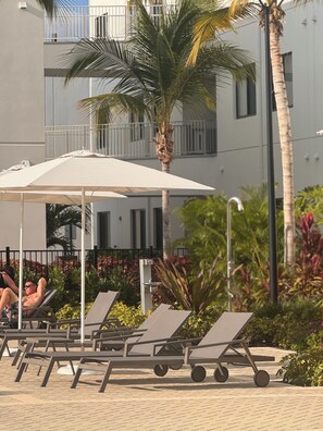 A poolside area with lounge chairs and umbrellas, palm trees, and a building in the background. - Governors Village Seven Mile Beach Corridor (Seven Mile Beach)