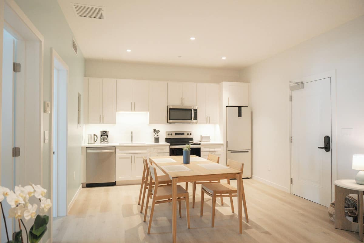 A modern kitchen with white cabinets, stainless steel appliances, and a wooden dining table.