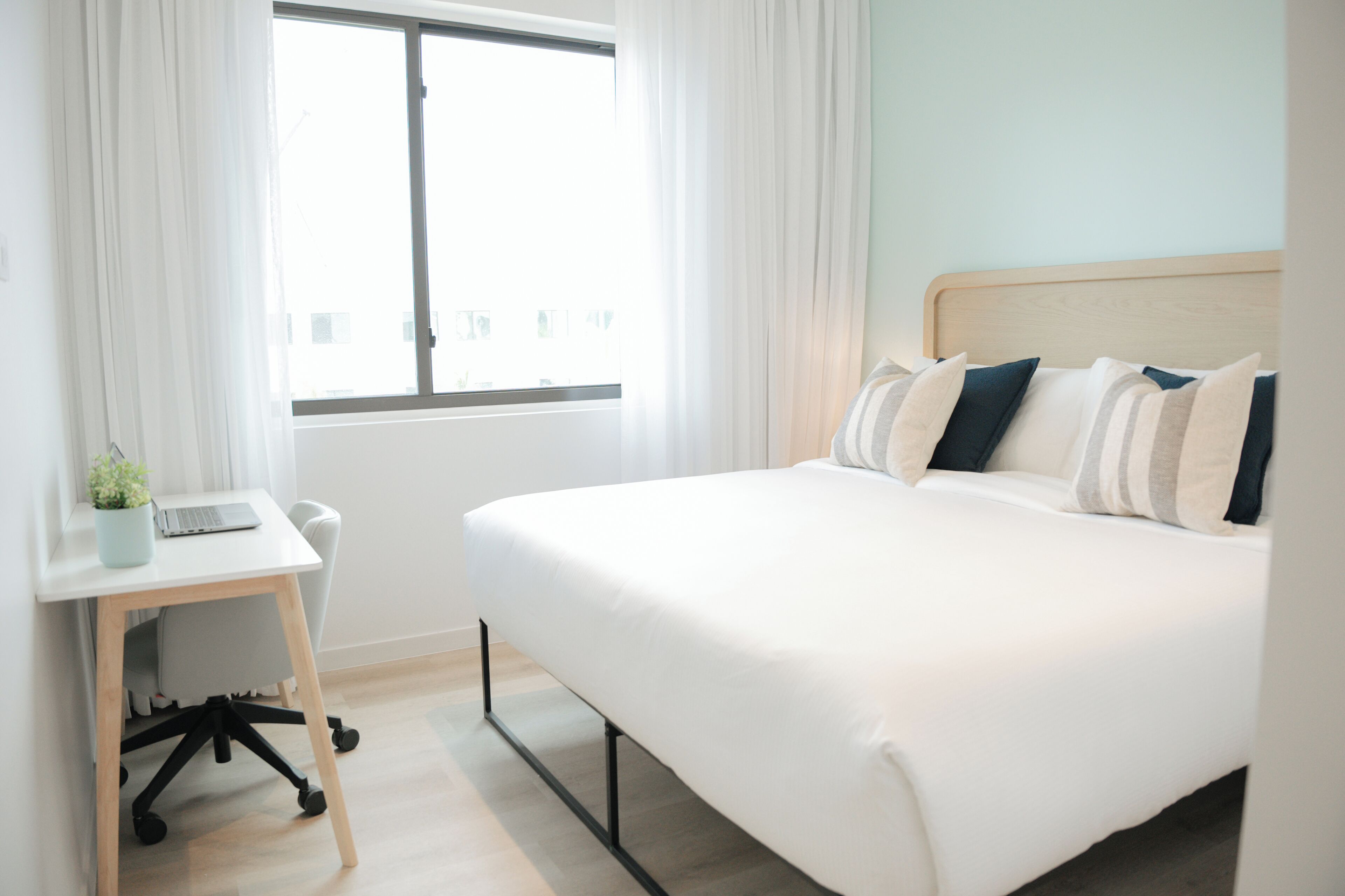 Una camera d'albergo con un letto, una scrivania con un portatile e una finestra con tende.