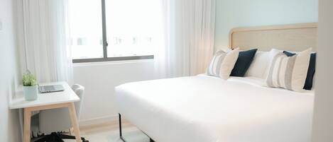 Una camera d'albergo con un letto, una scrivania con un portatile e una finestra con tende.
