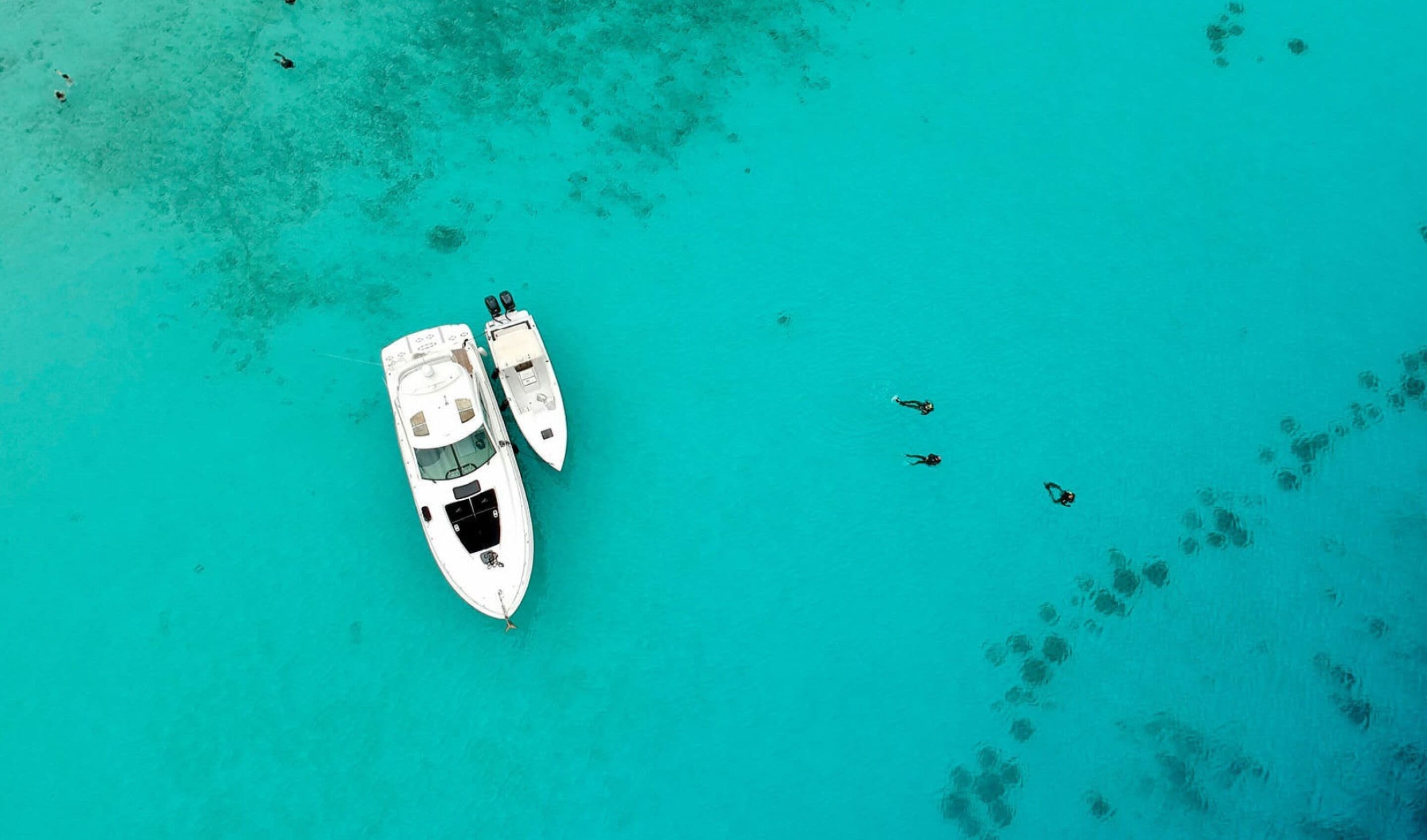An aerial view of a boat anchored in turquoise waters with a clear sky above.