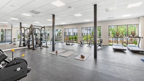 A spacious gym with various exercise equipment, large windows, and a view of greenery outside.
