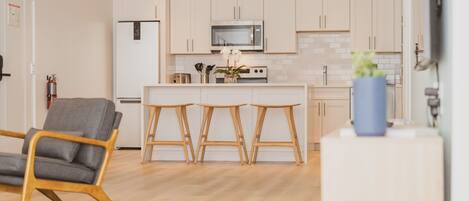 Una cocina moderna con armarios de tonos claros, un microondas y una isla central con taburetes.