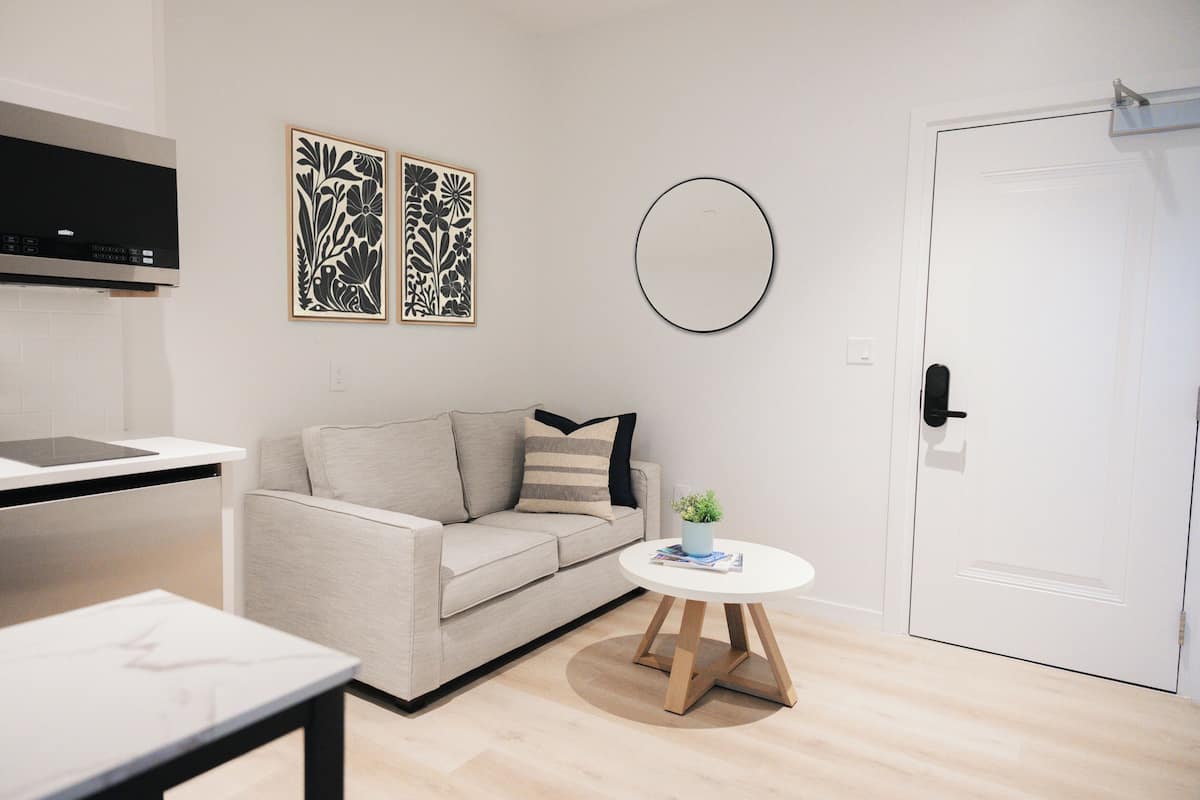 A modern living room with a sofa, a small round table with a plant, and a white door.