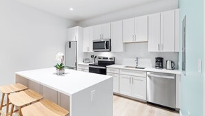 A modern kitchen with white cabinets, a central island with stools, a microwave, stove, and a dishwasher.