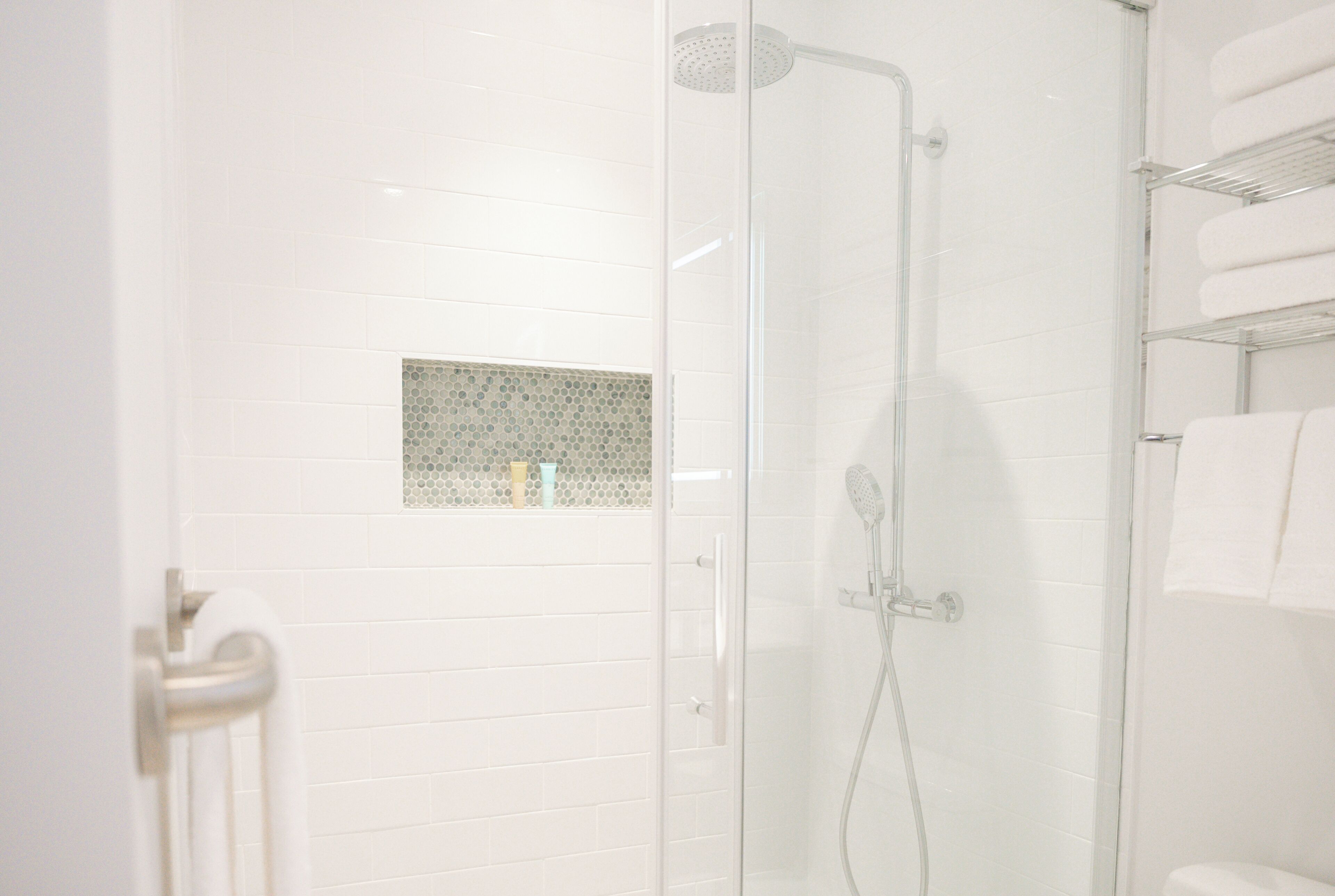 A modern bathroom with white tiles, a glass shower enclosure, and a towel rack.