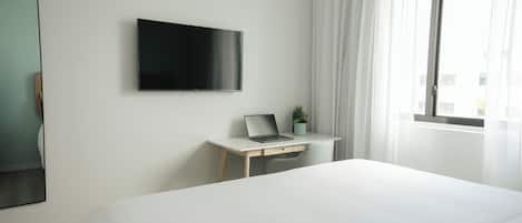 Una habitación de hotel con cama, escritorio con computadora portátil, televisor y ventana con cortinas.