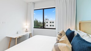A hotel room with a bed, a desk, and a window with curtains.