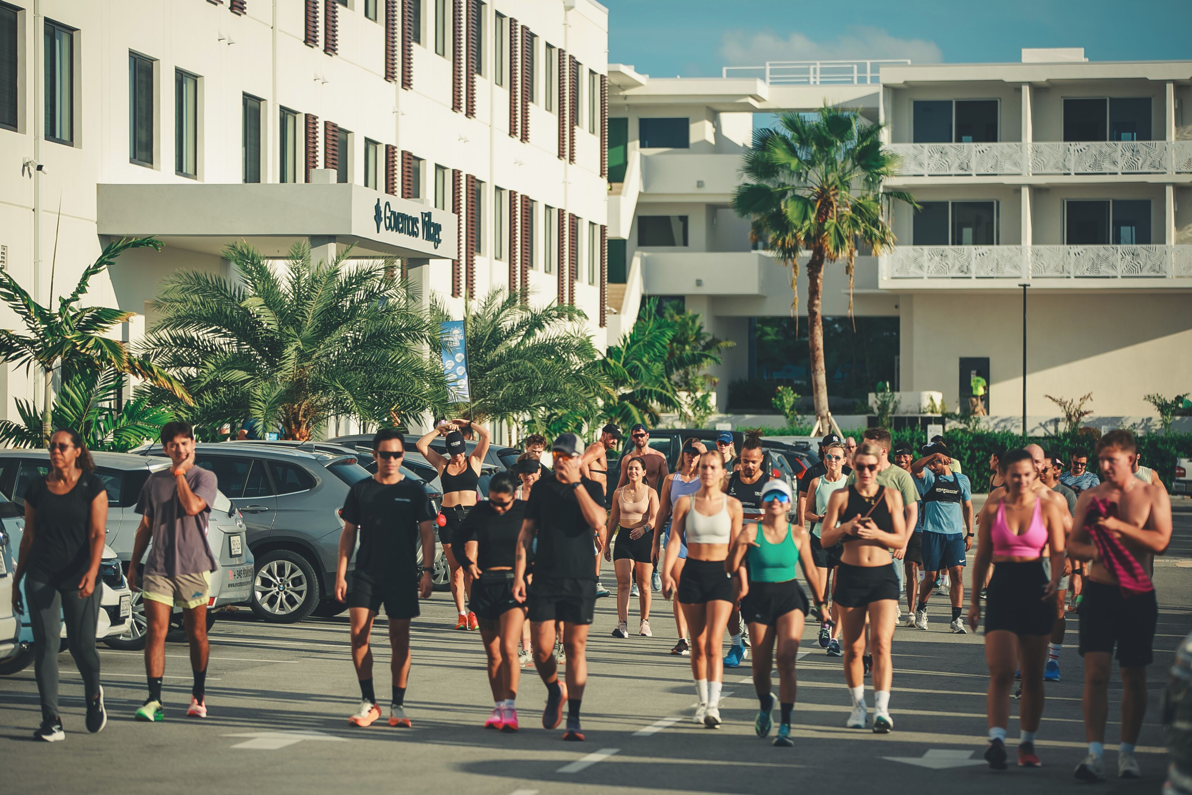 A group of people walking in a parking lot with buildings in the background.