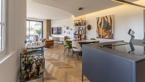 Ein modernes Wohnzimmer mit Fischgrätparkett, einem Glastisch und einem Essbereich mit einem großen Gemälde.