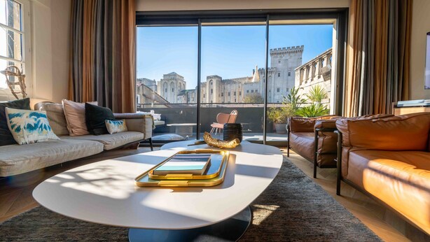 Ein modernes Wohnzimmer mit großem Fenster, einer Couch, einem Couchtisch und Blick auf historische Gebäude.