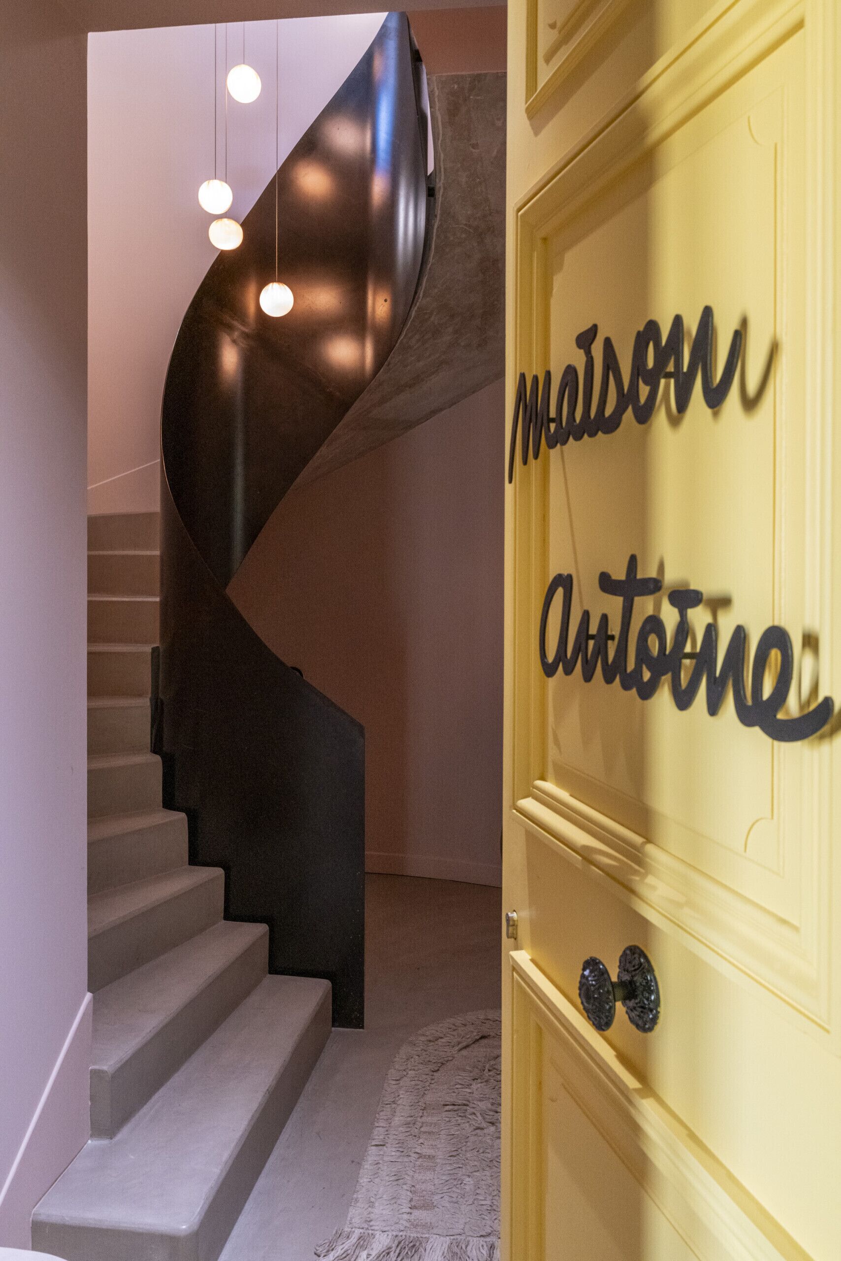 A spiral staircase with a modern design, leading to a door with a nameplate.