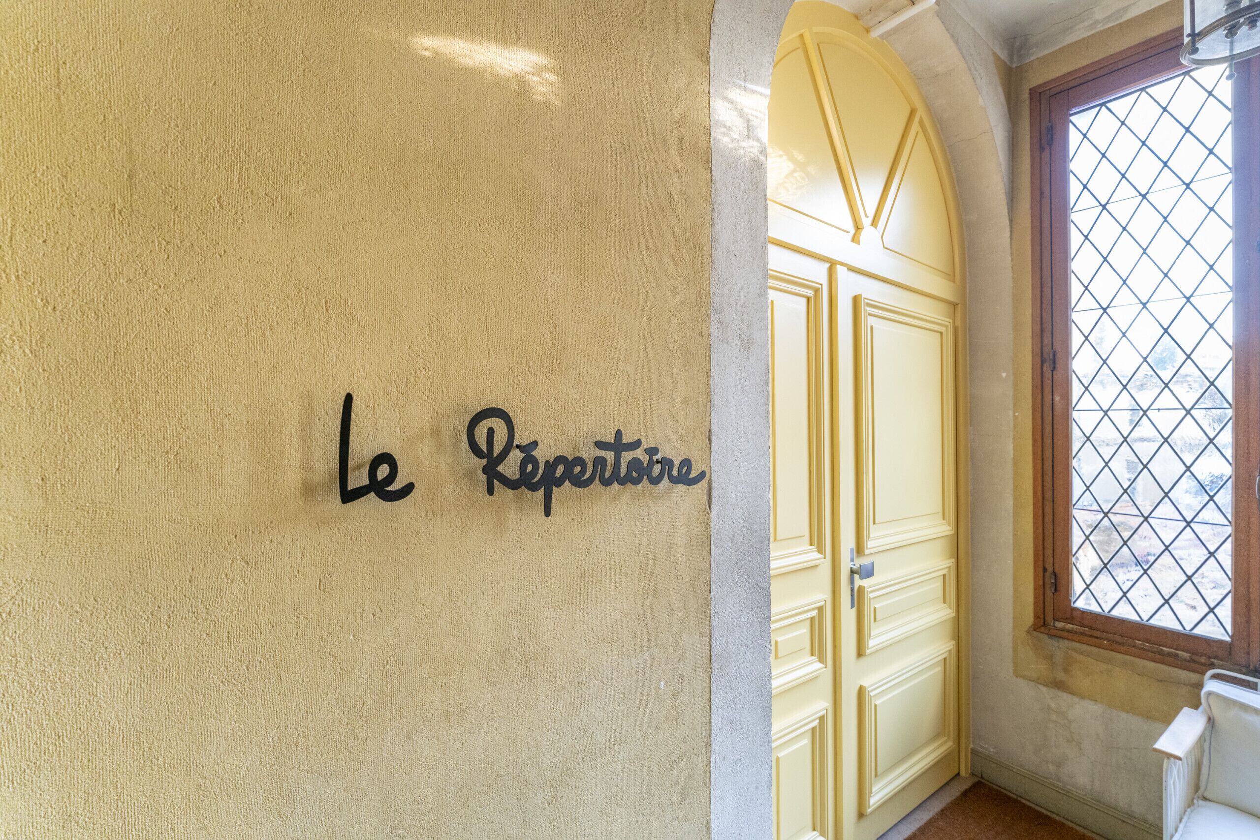 Una pared con el texto "Le Répertoire" y una puerta amarilla con una ventana.