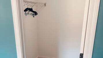 A small, empty walk-in closet with a white door, a beige carpet, and a metal drying rack with clothes.