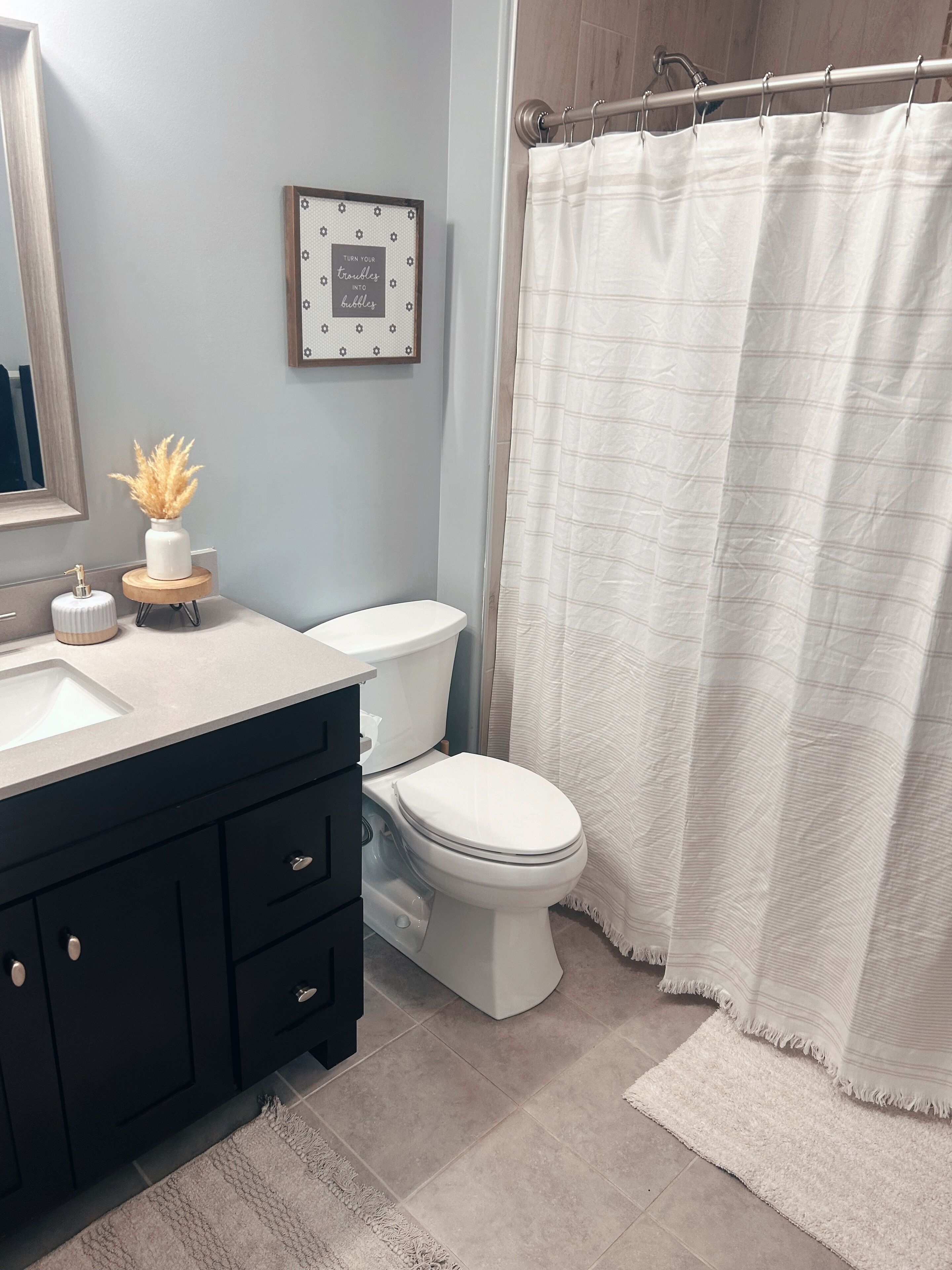 A bathroom with a white toilet, a sink with a wooden base, a mirror, and a framed quote on the wall.