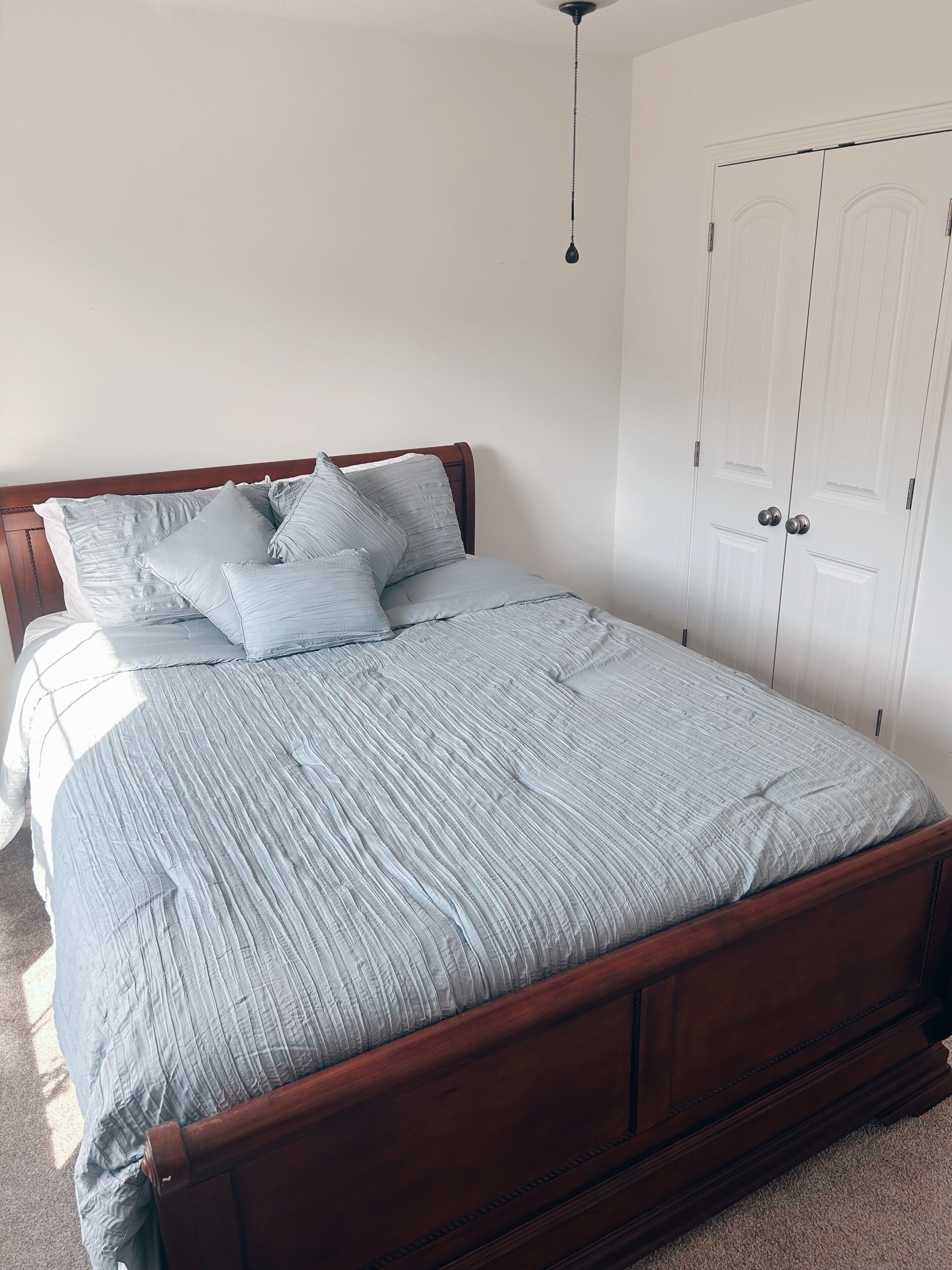 A bedroom with a wooden bed, grey bedding, and a white door.