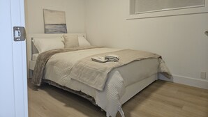 Een slaapkamer met een bed, een raam met zonwering, een deur en een aan de muur hangend kunstwerk.