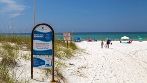 Een strandscène met een bord waarop waarschuwingen voor het strand en informatie over toegang voor hulpdiensten staan.