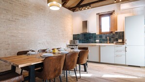 Comedor con una mesa de madera dispuesta para cuatro personas, rodeada de sillas marrones. Se ve una pared de ladrillo y una lámpara colgante.