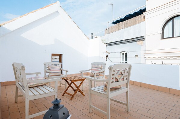 Une terrasse dotée de mobilier blanc, comprenant des chaises et une table, ainsi qu’une lanterne.